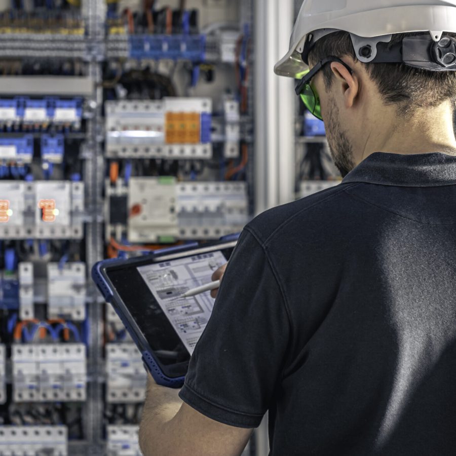 Man, an electrical technician working in a switchboard with fuses. Installation and connection of electrical equipment. Professional uses a tablet.
