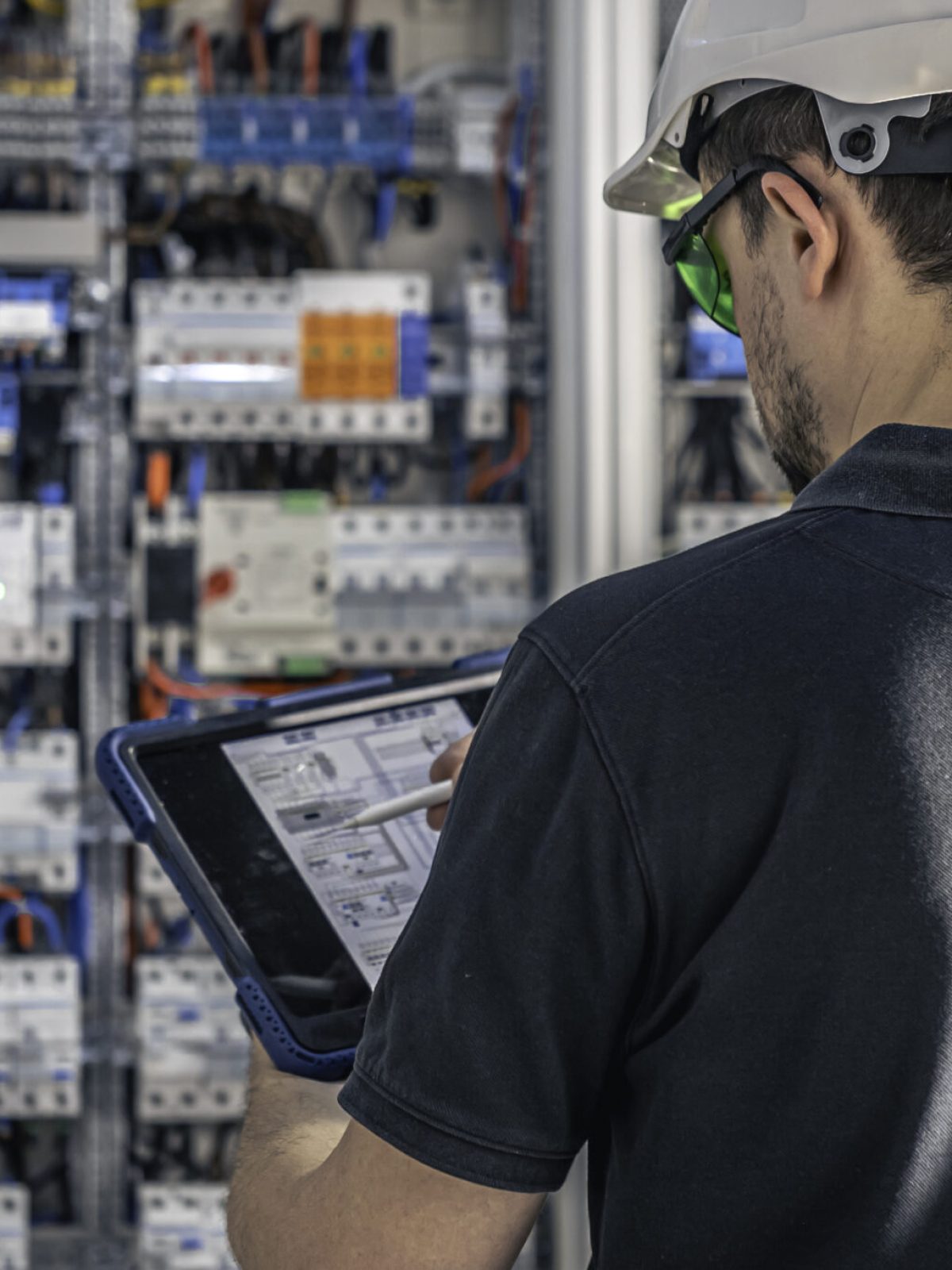 Man, an electrical technician working in a switchboard with fuses. Installation and connection of electrical equipment. Professional uses a tablet.